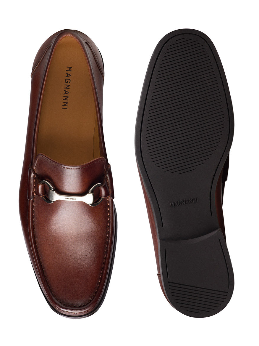 Magnanni Gentry in Cognac showcases a brown leather bit loafer with silver accents. One shoe is displayed from the top, revealing its elegant design, while the other shows a treaded sole. Crafted from supple leather, they provide excellent style and comfort for any occasion.