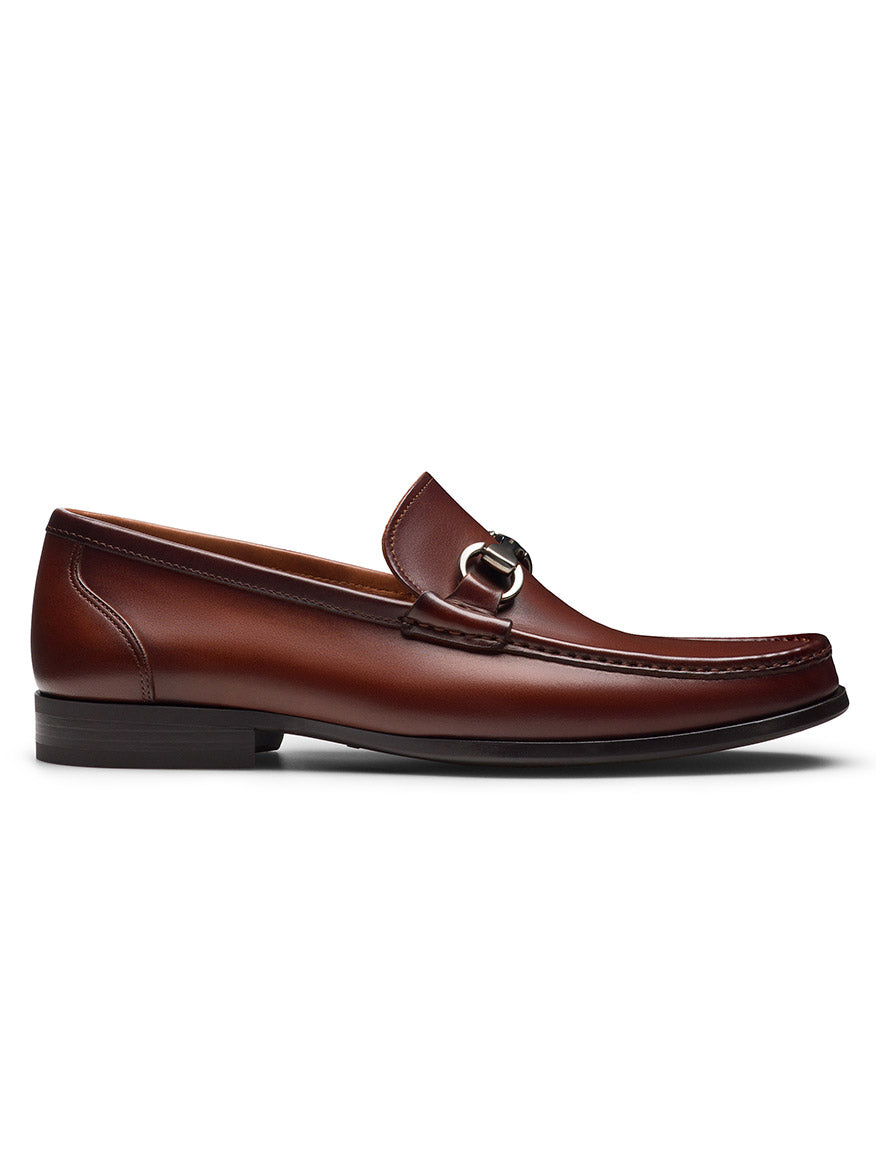 The Magnanni Gentry in Cognac is a brown leather bit loafer boasting a silver buckle, made from supple leather. It features a sleek design with a low heel, elegantly displayed against a white background.