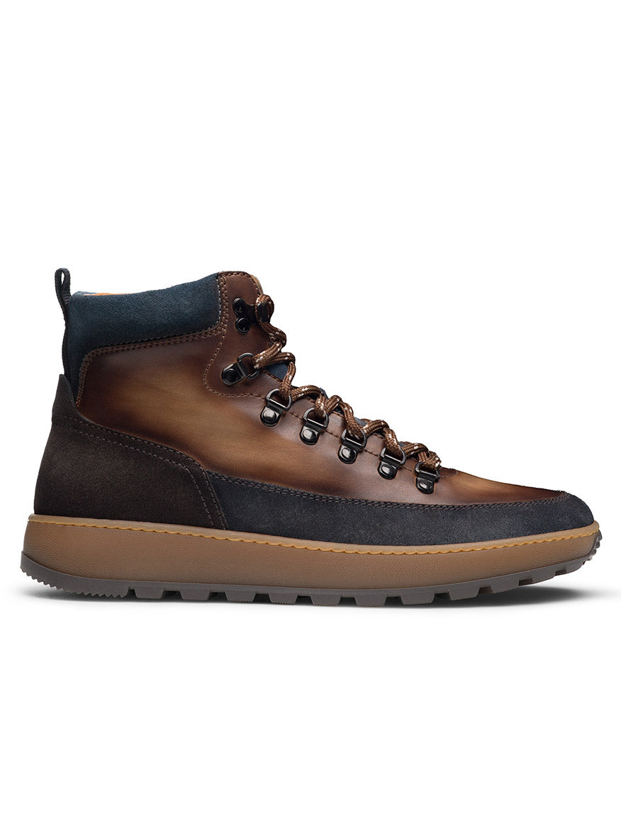 The Magnanni Borazo in Indigo/Brown is a leather hiker boot with metal eyelets, dark laces, and a tan rubber sole, combining rugged functionality and style. Shown from the side on a white background.