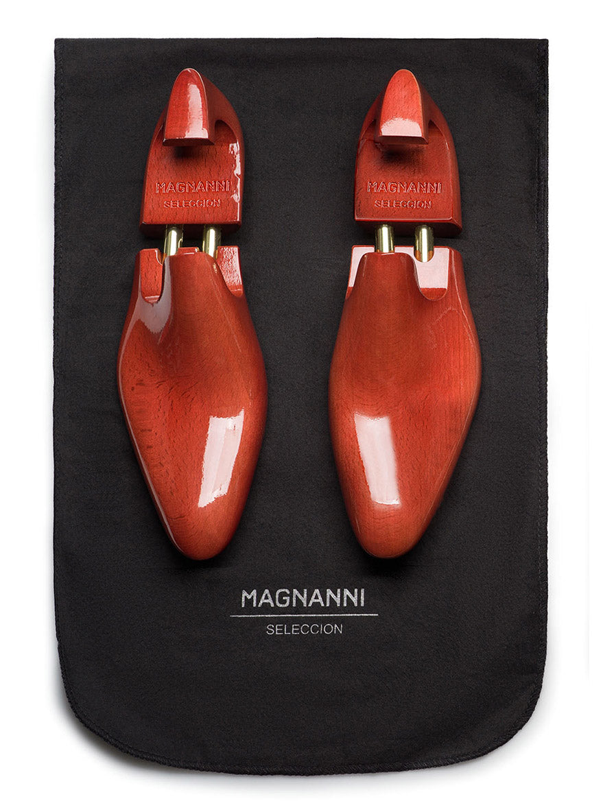 A pair of polished wooden shoe trees, symbols of craftsmanship, rest on a black branded fabric from the Magnanni Duke in Tabaco/Brown collection, exuding luxury.