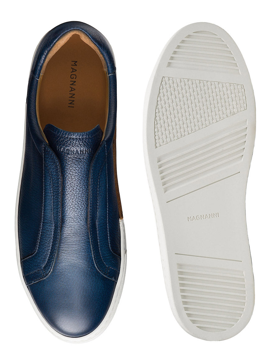 The Magnanni Gasol in Tumbled Navy features blue leather slip-ons with an elastic gore system for easy wear and white Artesano soles. One shoe shows the top view, while the other highlights its sole, both displaying the "Magnanni" brand on the insole and sole.