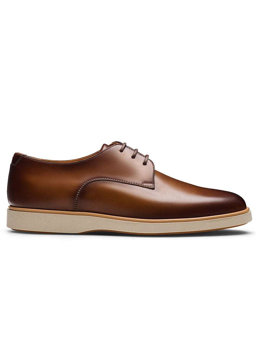 The Magnanni Leone II in Tabaco features a brown leather upper, plain toe derby design with laces, and a white rubber sole. Shown from the side against a white background, this hybrid dress shoe blends classic style with modern comfort.
