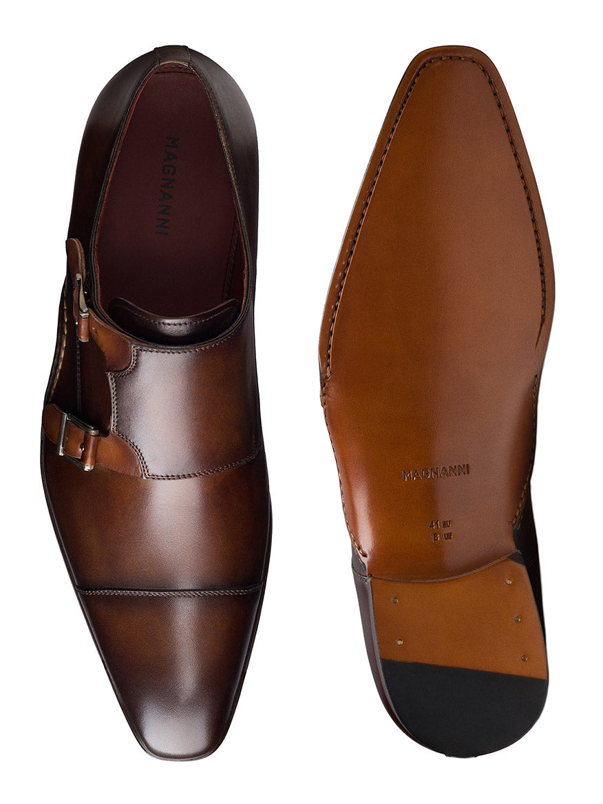 Magnanni Leros in Tabaco/Cuero are brown leather dress shoes with a classic monk strap and double buckles. One shoe is top-viewed; the other shows its Bologna construction, brand name, and size on the sole.