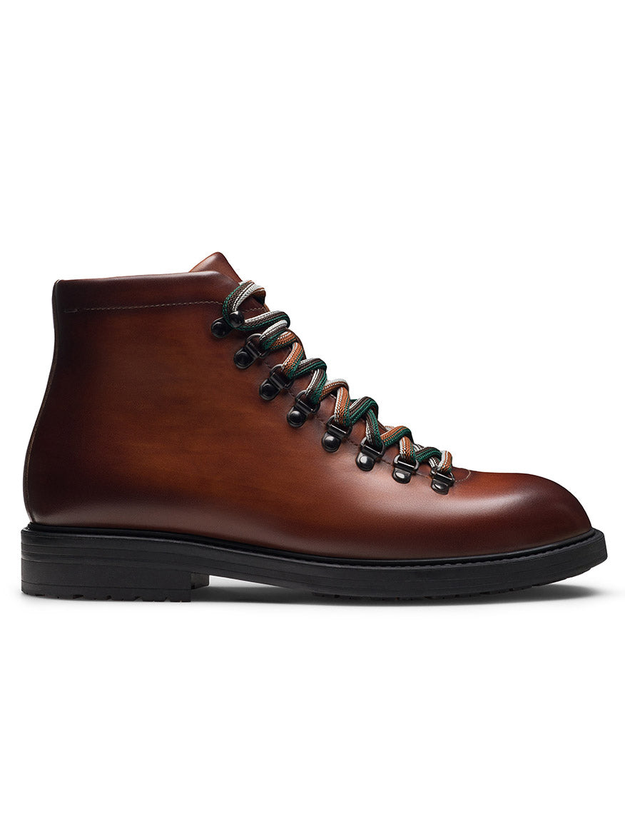 The Magnanni Montana X in Cognac is a brown leather fashion hiking boot with black and green laces, metal eyelets, and a black rubber sole, shown from the side.