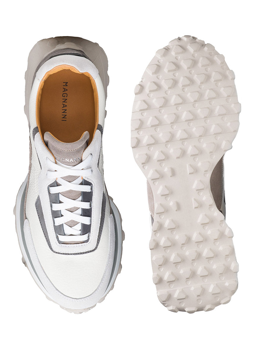 The Magnanni Onyx in White/Grey showcases a top and sole view of its luxurious design with jagged tread, gray and silver accents, and an orange interior branding.