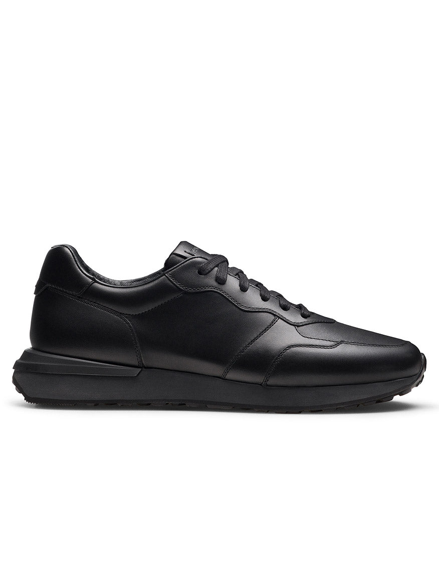 The Magnanni Syros in Black is a luxurious leather low-top sneaker featuring a lace-up closure, premium leather upper, and flat rubber sole. Shown in side profile on a white background.