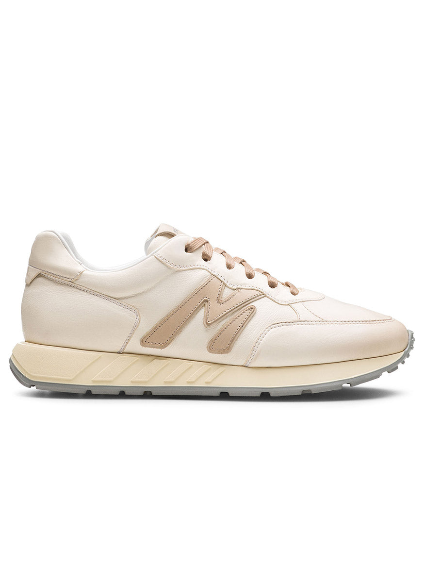 The Magnanni Yoki in White/Cream is a white sneaker with beige accents, a textured athletic-style sole, and an "M" logo on the side, ideal for those seeking a timeless look.