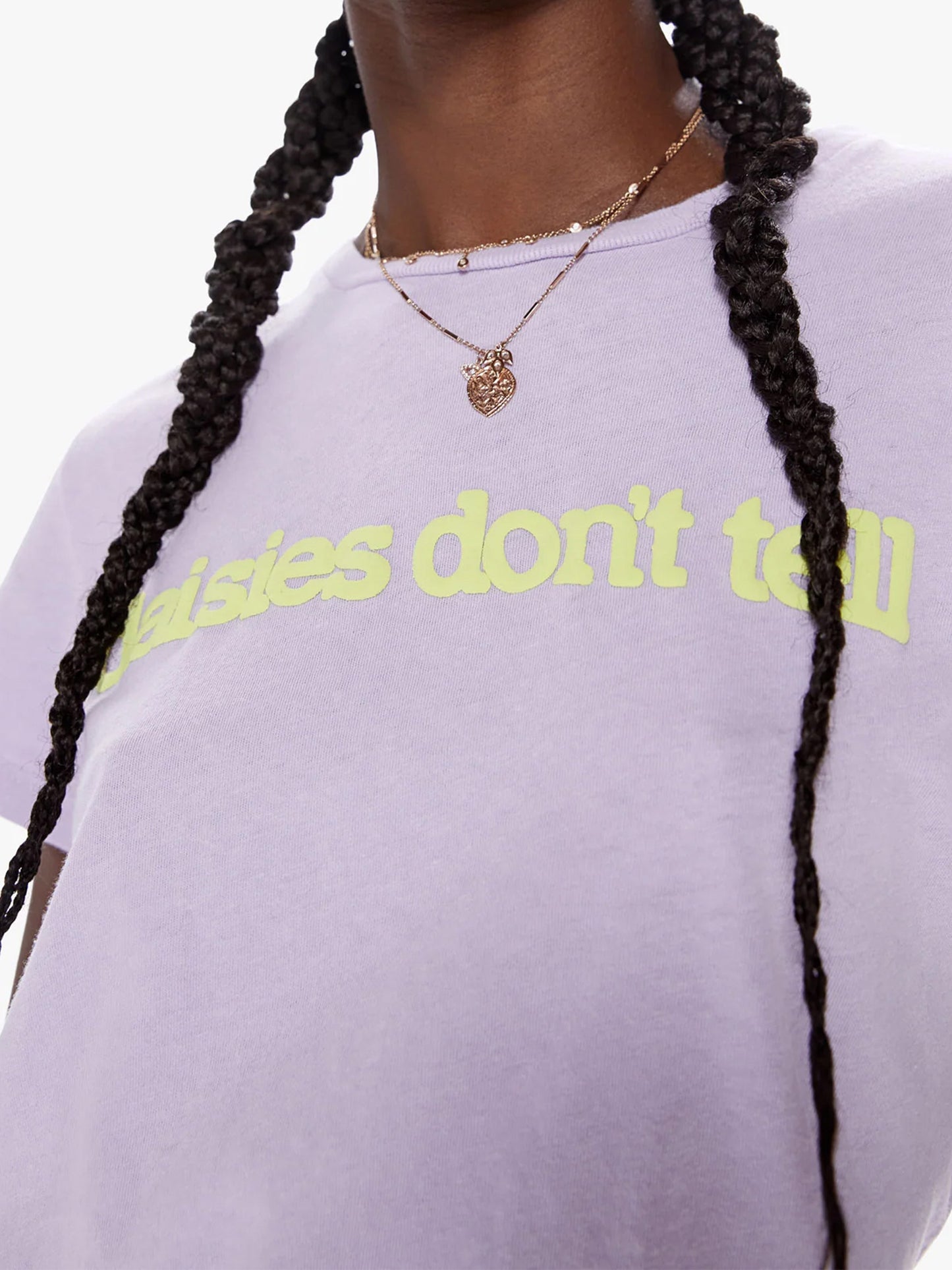 Close-up of a person wearing a Lavender Mother Denim The Boxy Goodie Goodie tee with the phrase "daisies don't tell" in green, accessorized with a heart-shaped necklace.