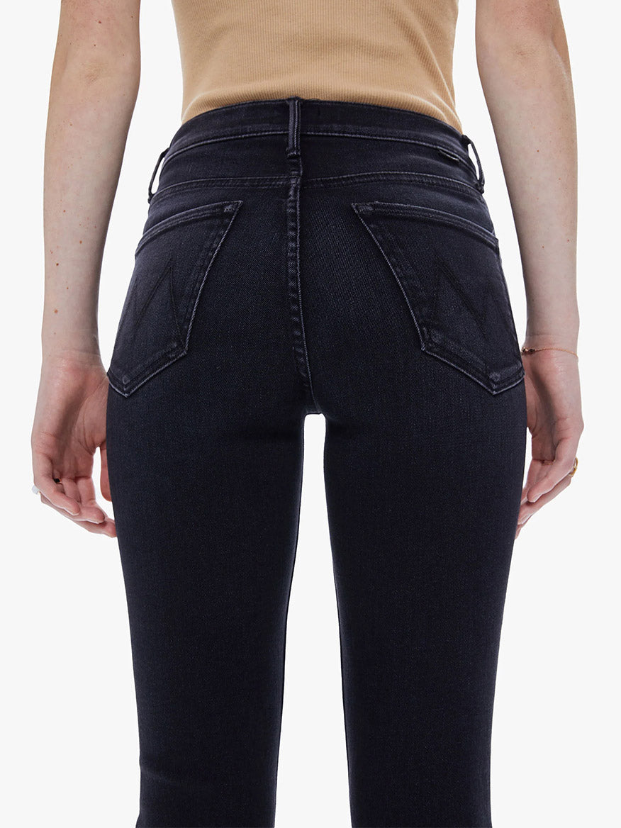 A person standing with their hands by their sides, showcasing the back view of a pair of Mother Denim The Dazzler Mid Rise Ankle in Deep End stretch denim jeans with distinctive pocket design.