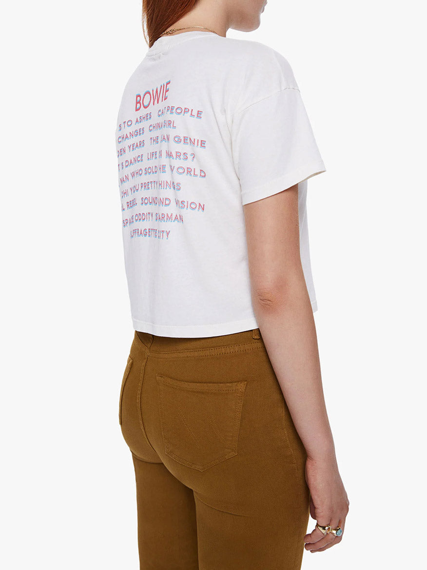 Rear view of a woman wearing a Mother Denim The Grab Bag Crop in Rebel Rebel tee from the David Bowie capsule collection, paired with brown trousers.