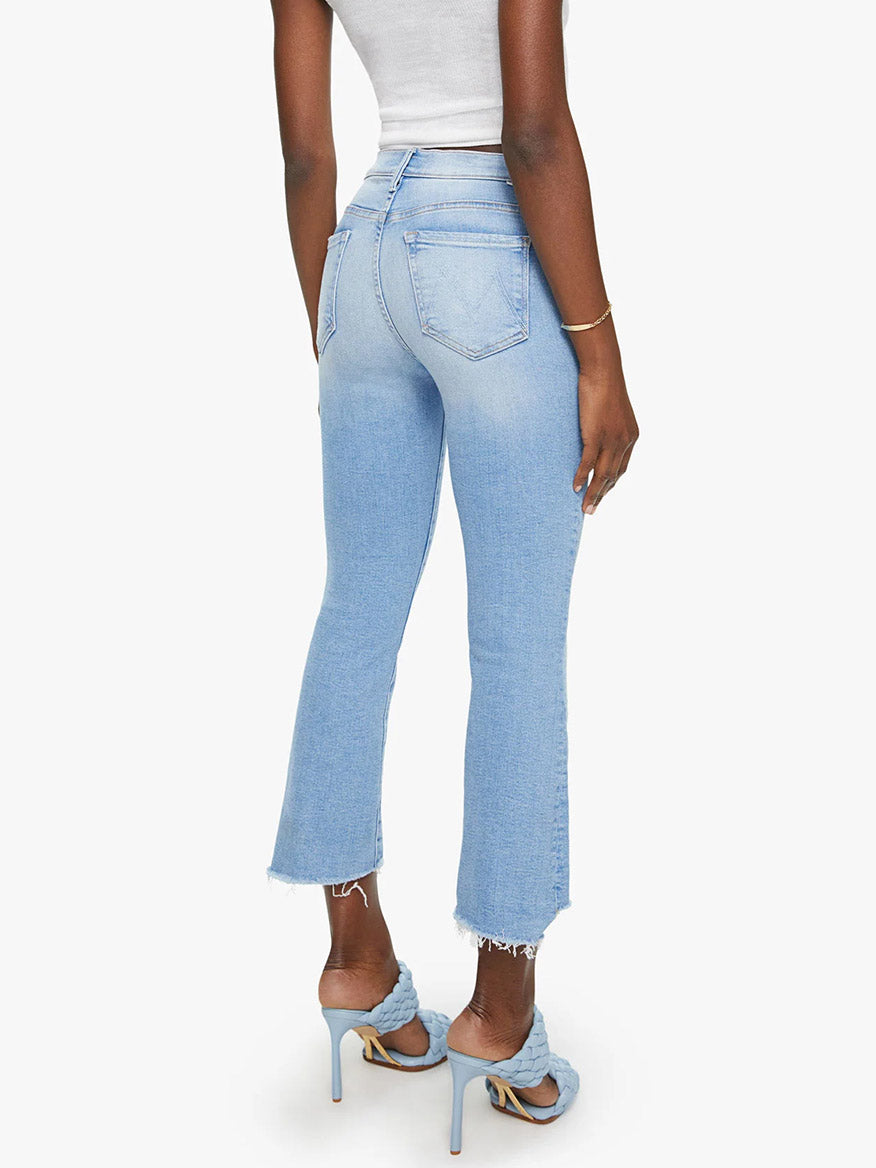Rear view of a woman wearing Mother Denim The Insider Crop Step Fray in Limited Edition jeans with a frayed step-hem and blue high heels.