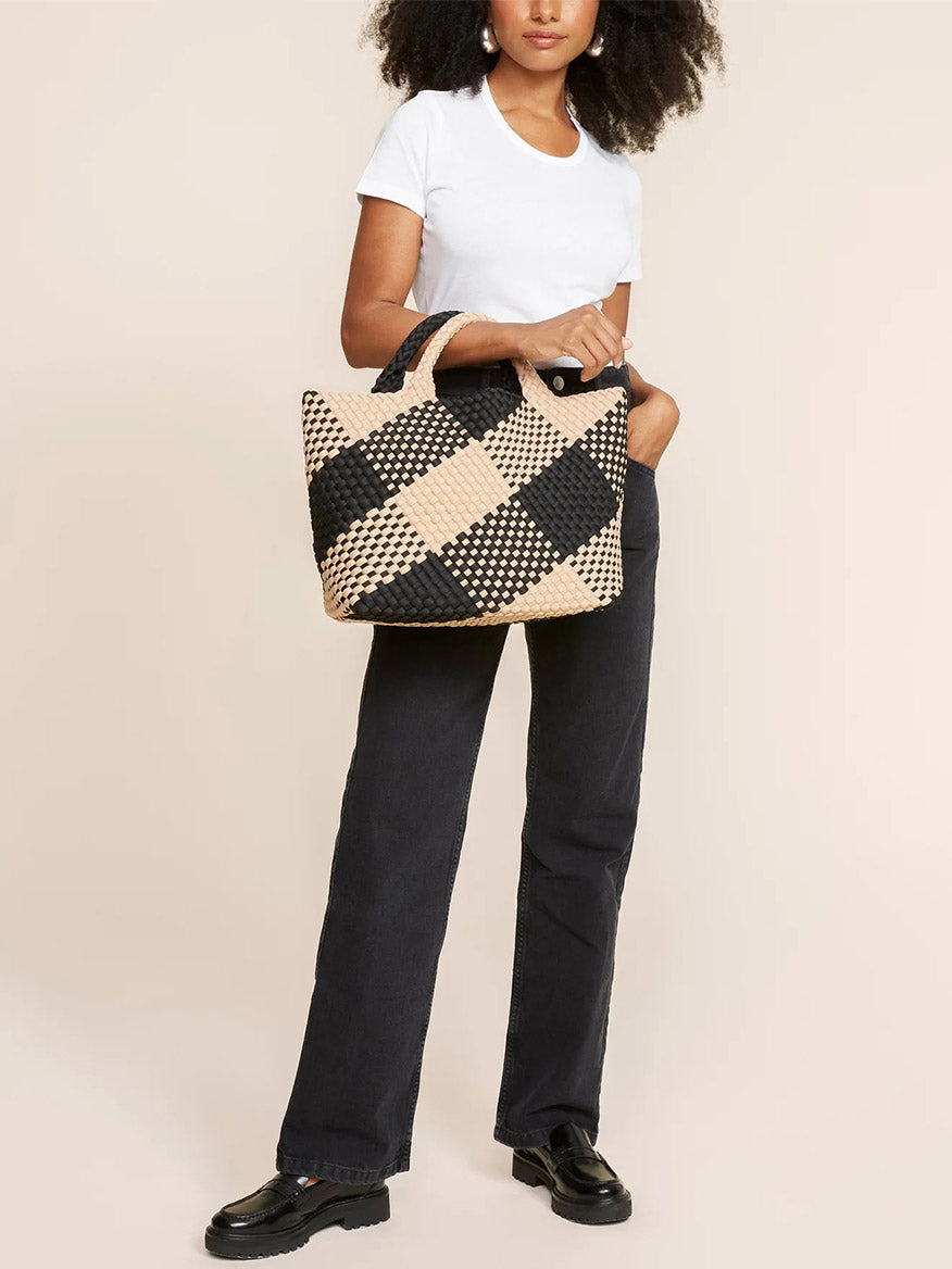 A woman in a white t-shirt and black jeans holding a large Naghedi St. Barths Medium Tote in Plaid Cabana.