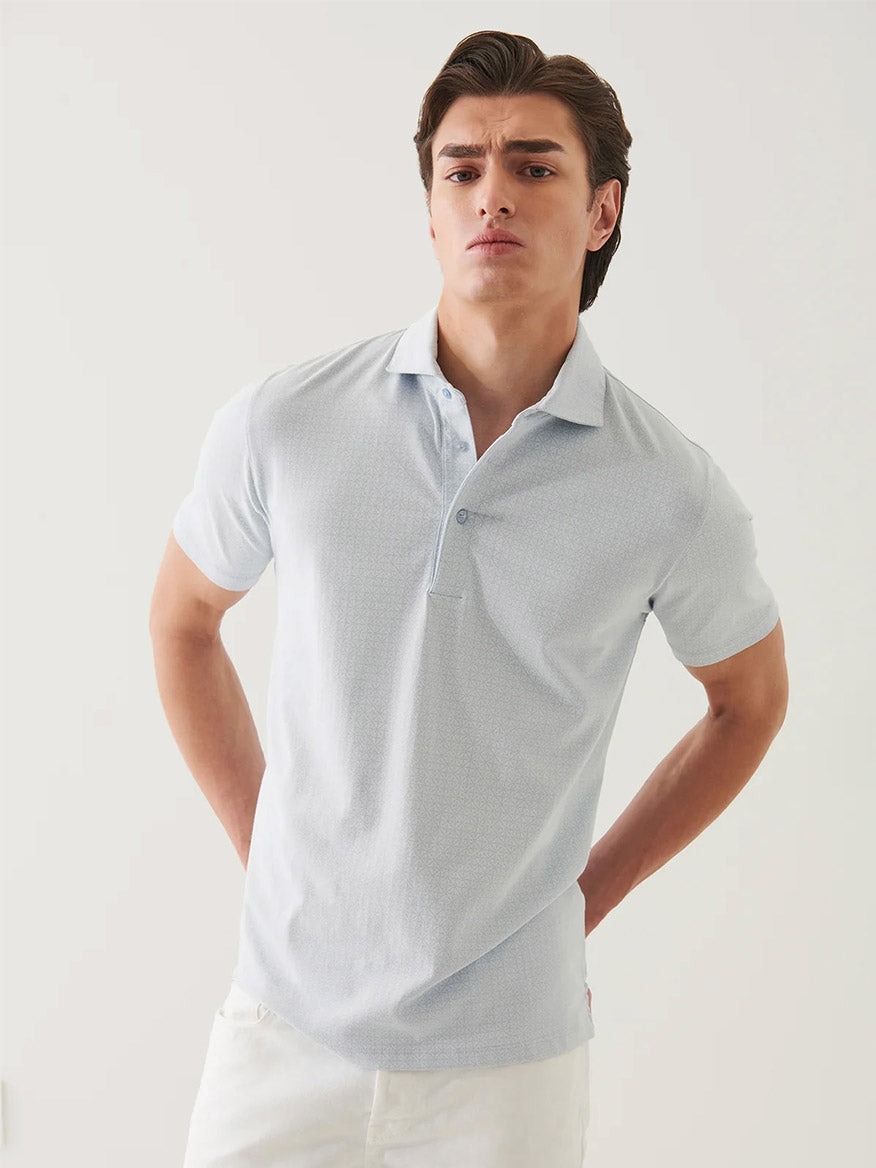 A young man wears the Patrick Assaraf Pima Cotton Stretch Printed Polo in Blue Ice with white pants, standing against a plain white background.