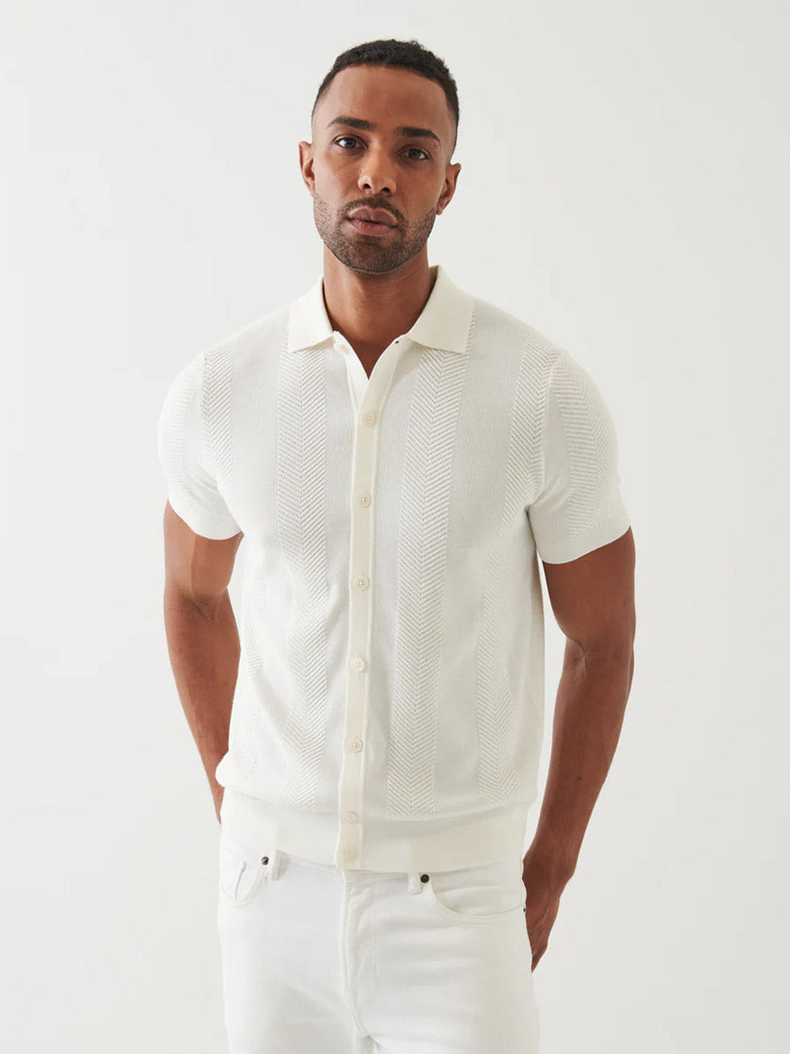 A man wears the Patrick Assaraf Cotton Cashmere Blend Knit Shirt in White and white pants, standing against a plain white background, facing the camera with a neutral expression.