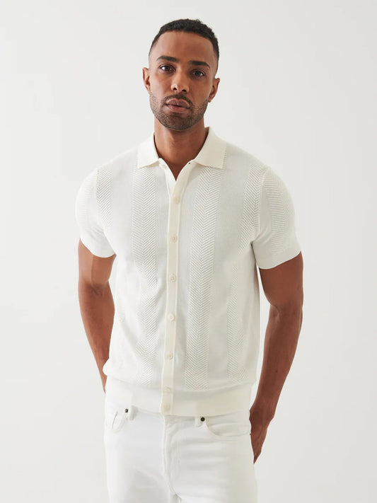 A man wears the Patrick Assaraf Cotton Cashmere Blend Knit Shirt in White and white pants, standing against a plain white background, facing the camera with a neutral expression.