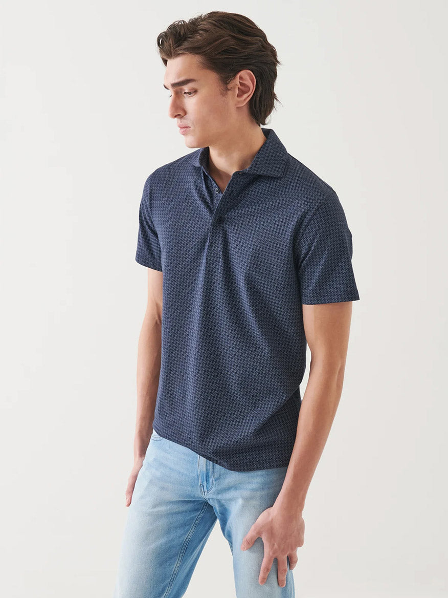 A man stands against a plain background wearing the Patrick Assaraf Pima Cotton Stretch Printed Polo in Midnight and light blue jeans, looking to his left.
