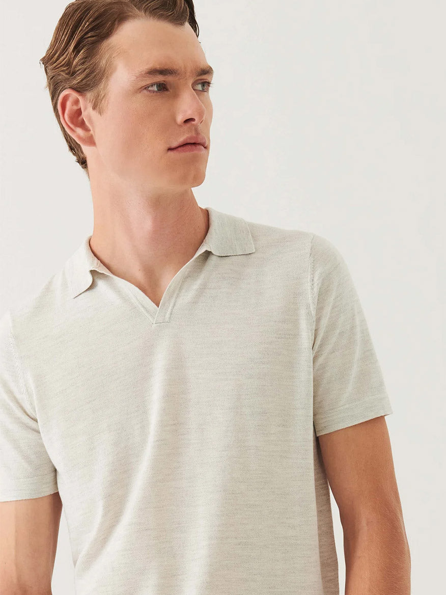 A man with short brown hair wears the Patrick Assaraf Cotton Cupro Open Polo in Drizzle, featuring a light beige hue and open collar, as he looks to his left against a plain background.