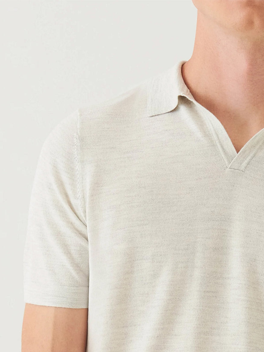 A person wears the Patrick Assaraf Cotton Cupro Open Polo in Drizzle, a light beige short-sleeve knit shirt with an open collar, displayed from shoulders to mid-torso against a plain background—perfect for versatile styling.