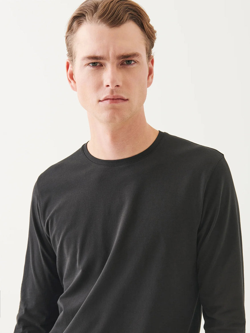 A man with light skin and short light brown hair wears the Patrick Assaraf Pima Cotton Stretch Long Sleeve T-Shirt in Black and looks directly at the camera against a white background.