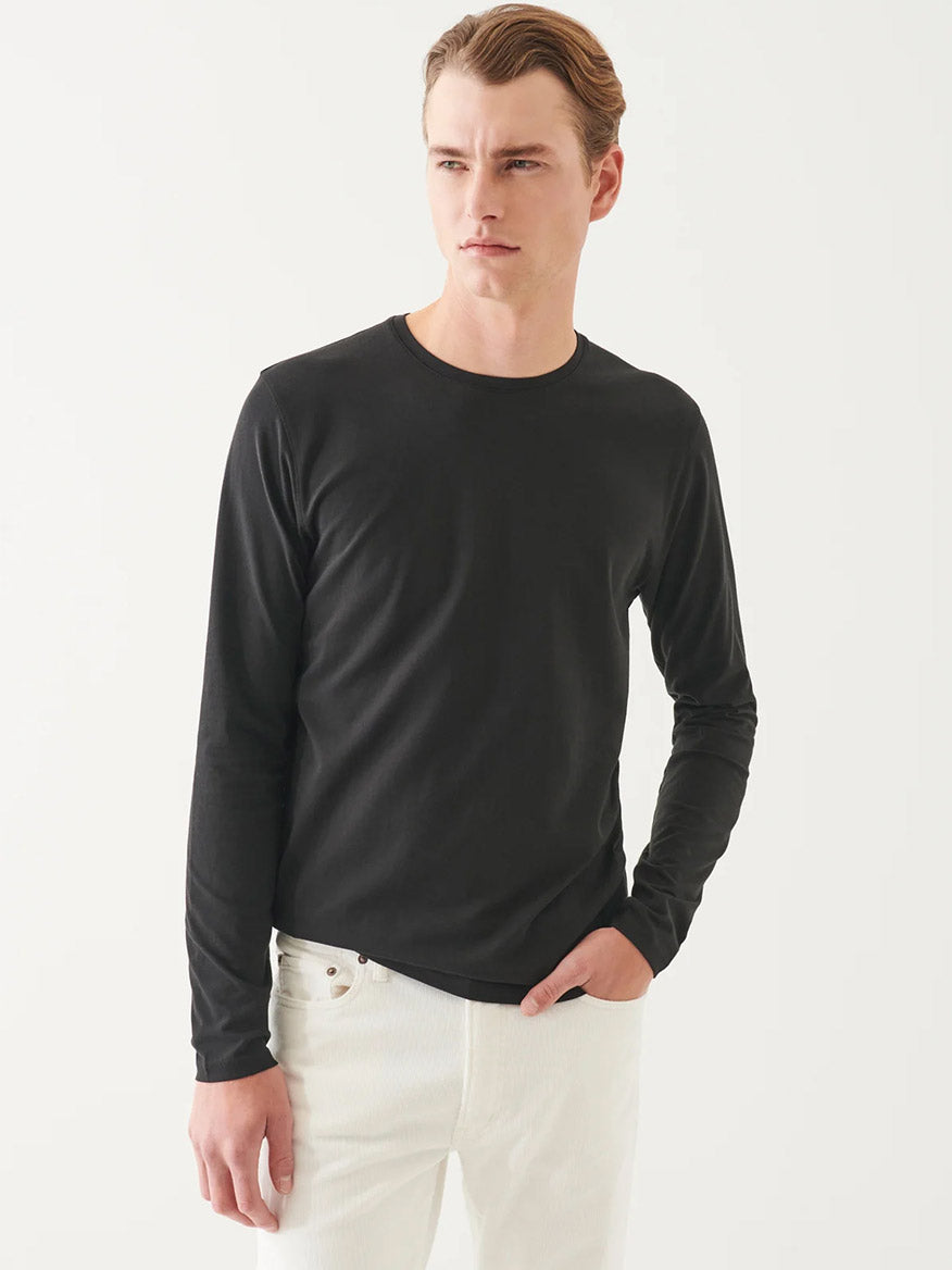 A man wearing the Patrick Assaraf Pima Cotton Stretch Long Sleeve T-Shirt in Black and white jeans stands against a plain white background, looking to the side.