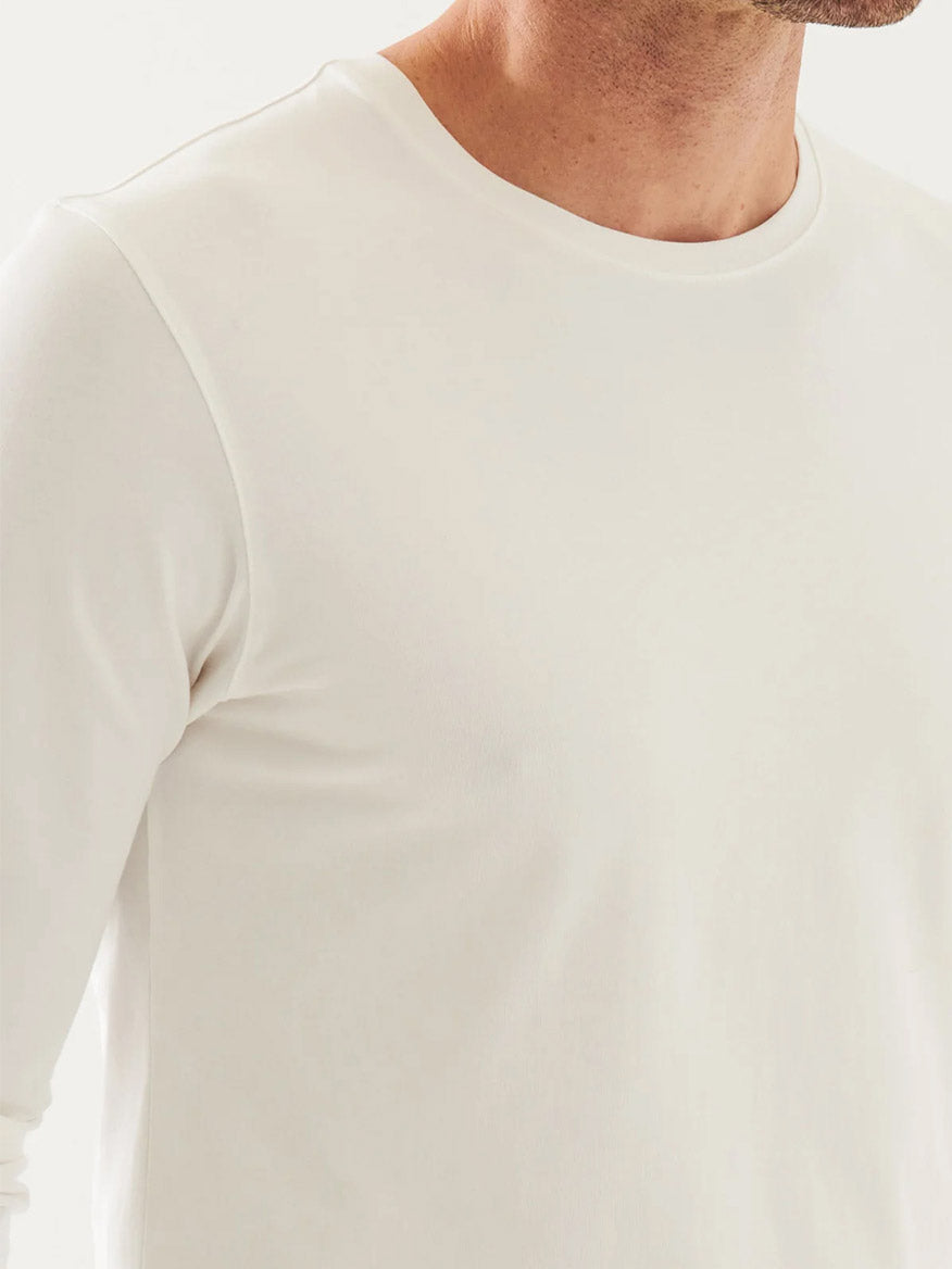 A person wears the Patrick Assaraf Pima Cotton Stretch Long Sleeve T-Shirt in White, showcasing its soft luxury fabric. The image captures the upper torso, neck, and jawline, highlighting the shirt's simplicity and premium quality.