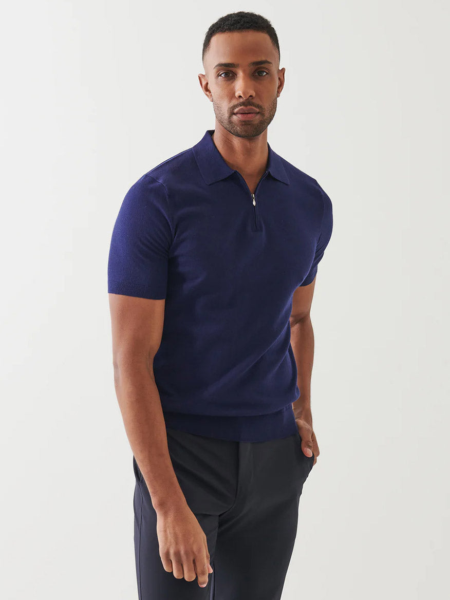 A man stands against a plain background wearing the Patrick Assaraf Cotton Cashmere Quarter Zip Polo in Navy with short sleeves and dark pants, highlighting its versatile style while looking directly at the camera.