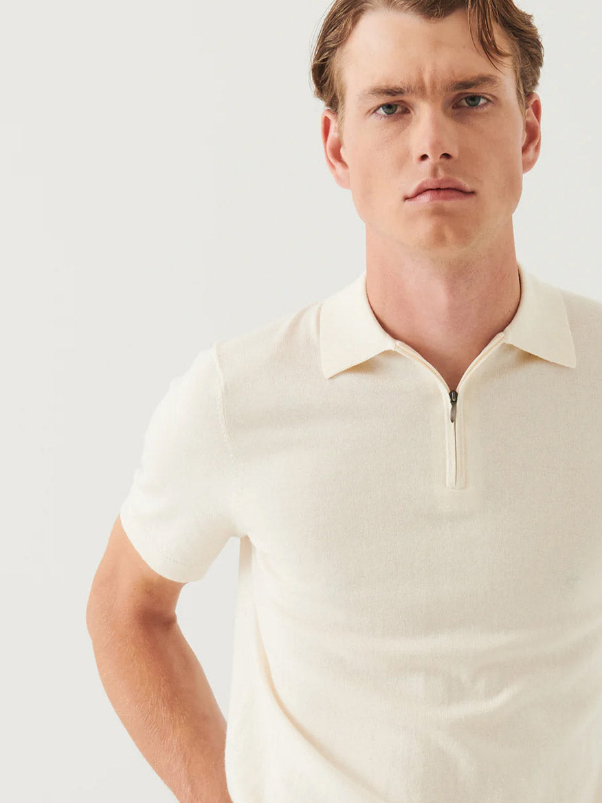 A man stands against a plain light background wearing the Patrick Assaraf Cotton Cashmere Quarter Zip Polo in Off White, featuring short sleeves and crafted from premium fabric.