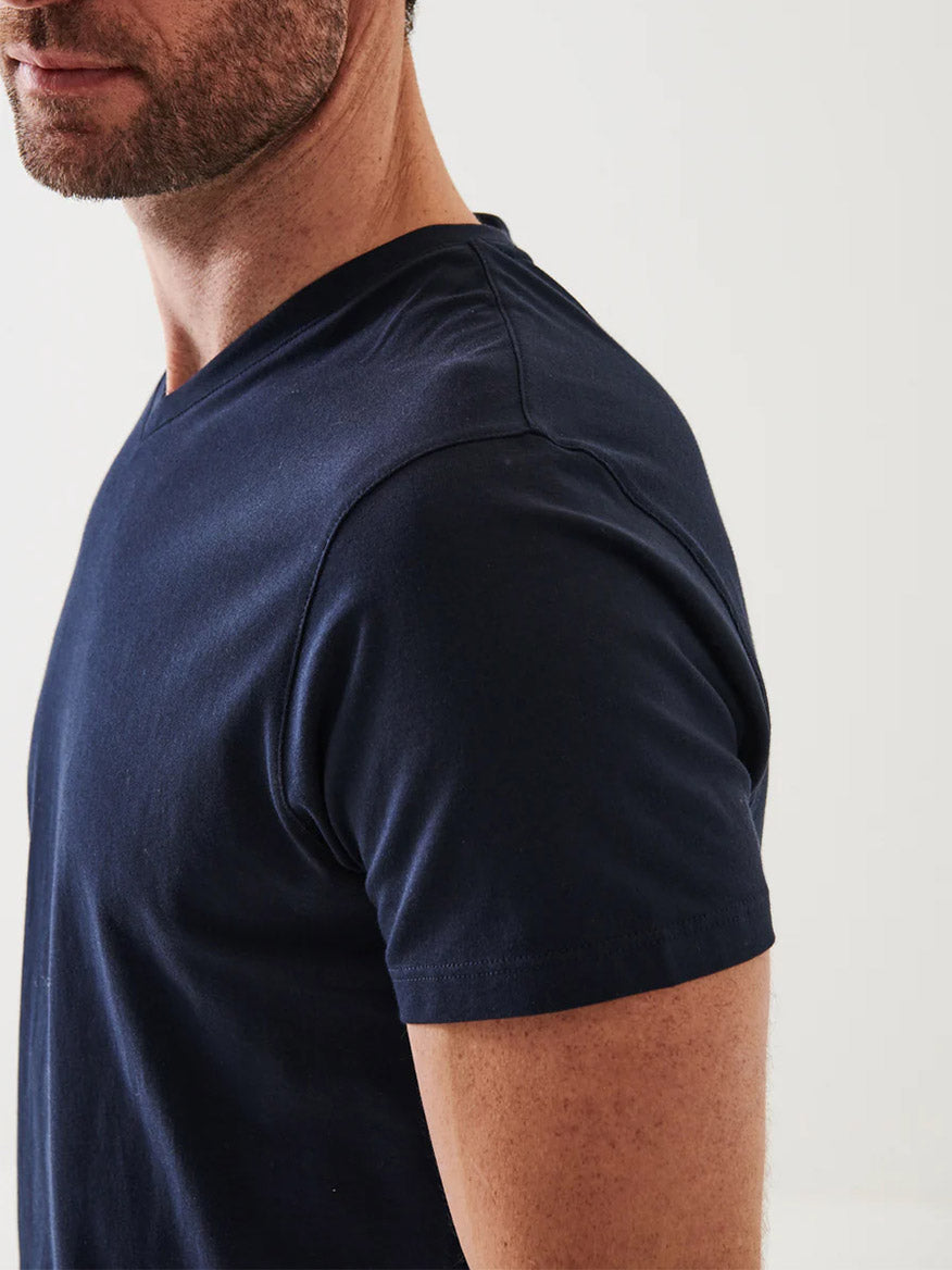 A man with short facial hair models the Patrick Assaraf Pima Cotton Stretch V-Neck T-Shirt in Midnight, standing angled to the side against a light background.