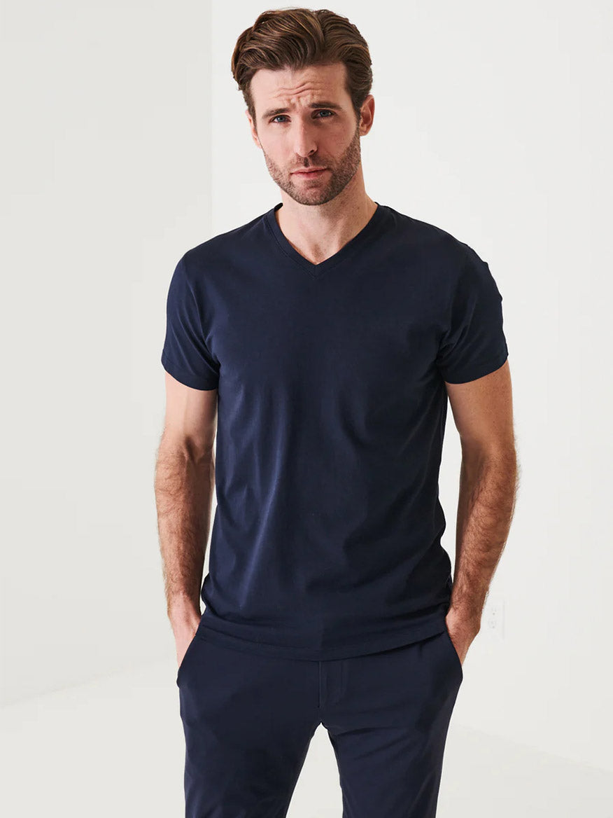 Man with light brown hair wearing a Patrick Assaraf Pima Cotton Stretch V-Neck T-Shirt in Midnight and matching pants, stands against a white background with hands in pockets, exuding timeless style.