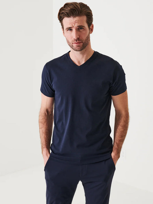 Man with light brown hair wearing a Patrick Assaraf Pima Cotton Stretch V-Neck T-Shirt in Midnight and matching pants, stands against a white background with hands in pockets, exuding timeless style.