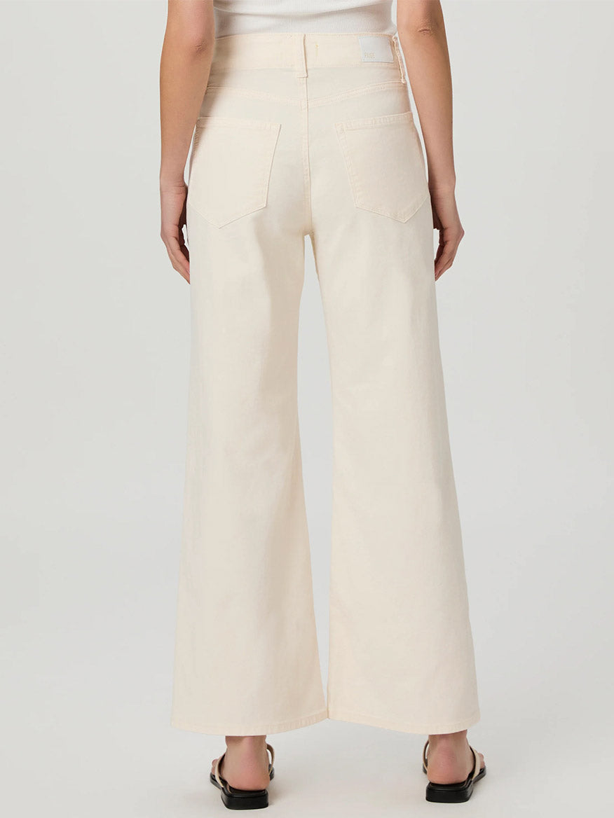 A person is wearing the Paige Ari Wide Leg Pant in Quartz Sand, paired with black sandals, viewed from the rear.