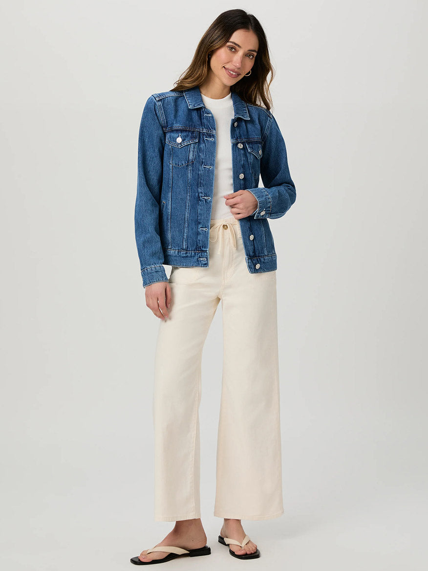 Woman in a super soft denim jacket over a white shirt and Paige Ari Wide Leg Pant in Quartz Sand, standing gracefully against a plain background.