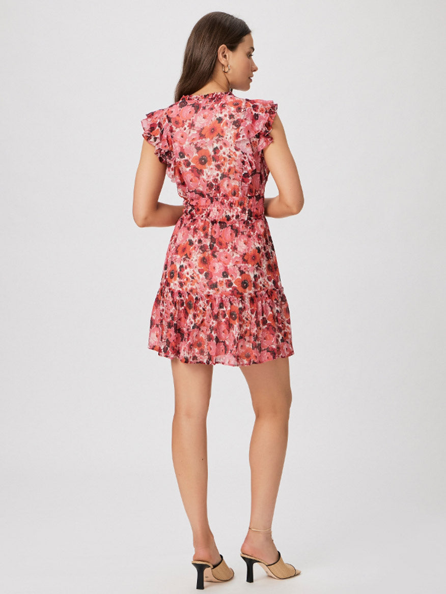 A woman wears a Paige Muriel Dress in Bissou Floral Multi with ruffles on the sleeves and stands facing away, showcasing the back of the dress and her brown hair tied up.