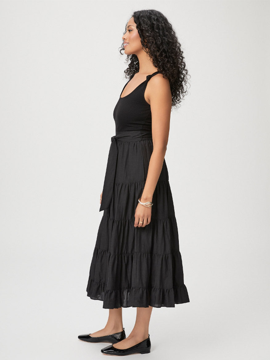 A woman in a Paige Samosa Dress in Black stands sideways with her eyes closed, wearing black ballet flats.