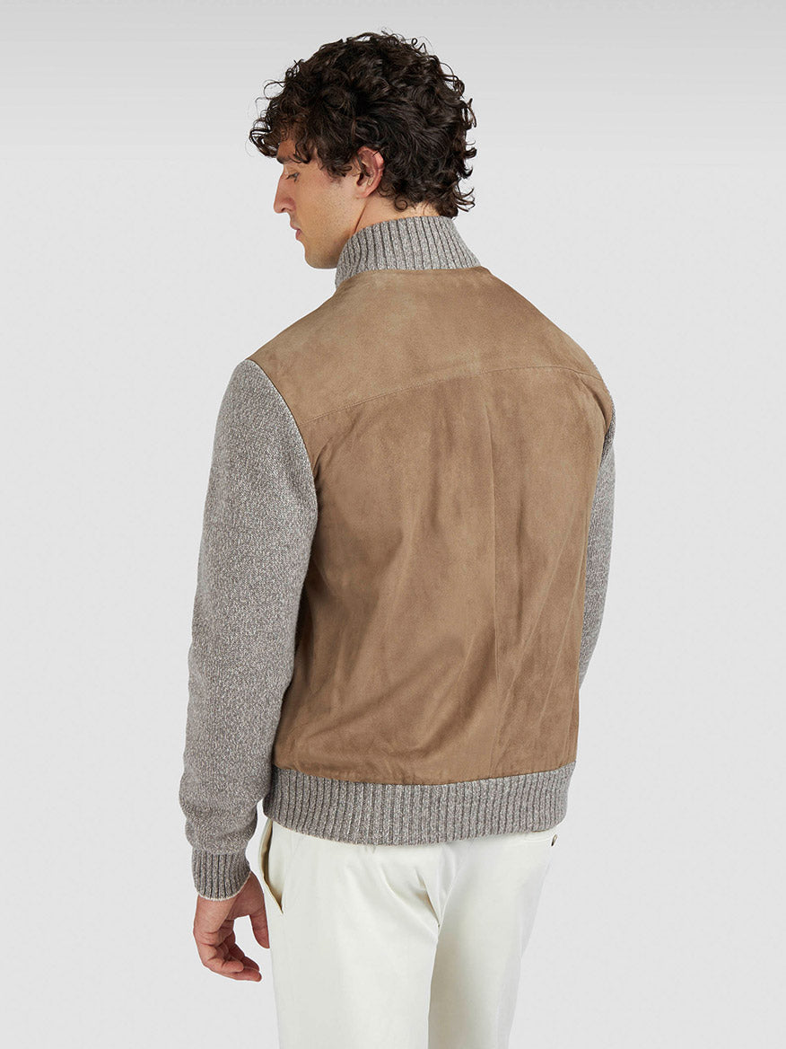 A man faces away, wearing the Paul & Shark Hybrid Zip-Up Cardigan in Natural with gray knit sleeves and collar, paired with white pants, against a plain light background.