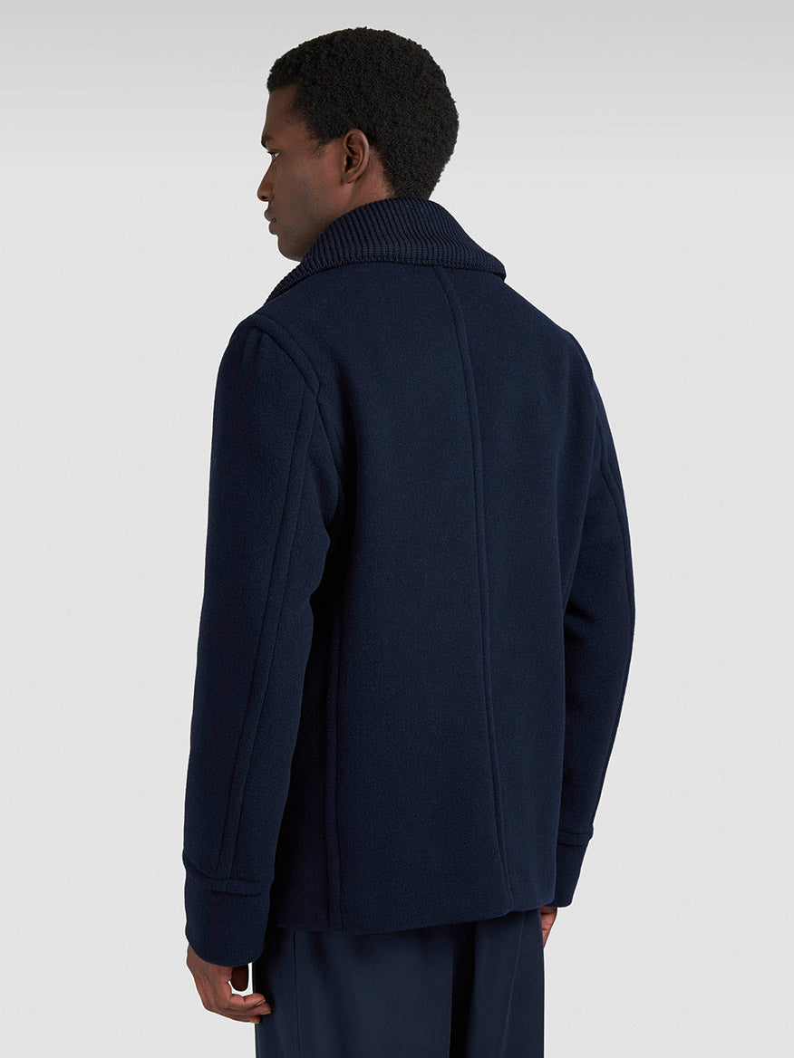 A man faces away while wearing the Paul & Shark Peacoat in Wool & Cashmere in Navy, featuring a wide collar and double-breasted closure, paired with dark trousers against a plain light background.