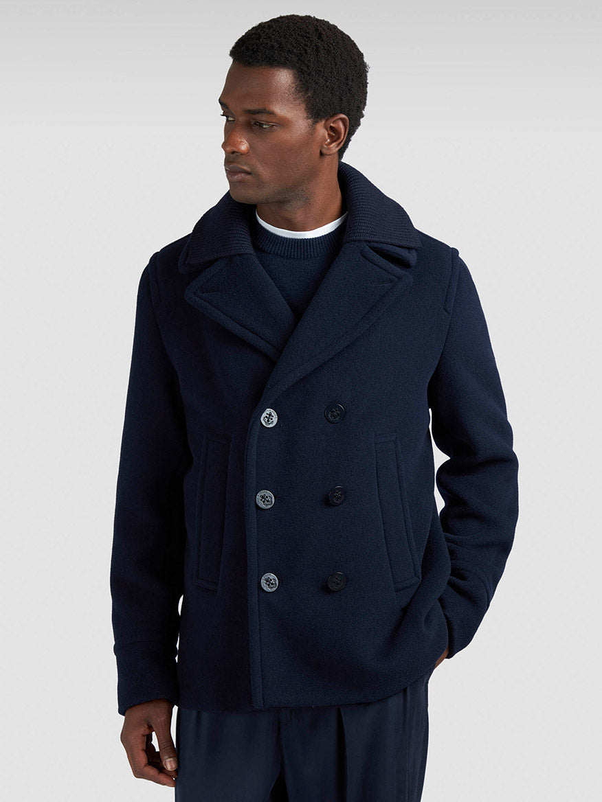A man wears a Paul & Shark Peacoat in Wool & Cashmere in Navy over a navy sweater and dark trousers, standing against a plain light background and looking to his left.