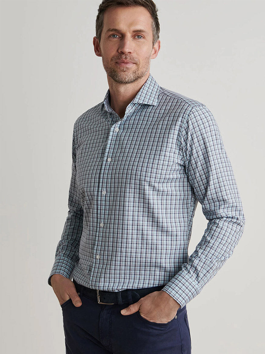 A man stands with hands in pockets, wearing the Peter Millar Abetone Cotton Sport Shirt in Blue Frost and dark pants against a plain light background.