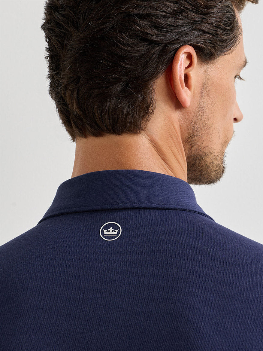 Man shown from behind wearing the Peter Millar Albatross Cotton Blend Piqué Polo in navy, featuring a small white crown logo on the upper back.