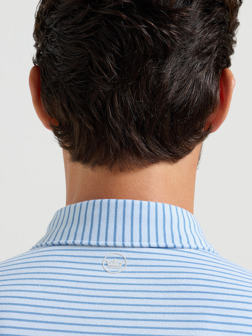 The back view of a person with dark hair wearing the Peter Millar Albatross Stripe Cotton-Blend Piqué Polo in Blue Brisk, featuring light blue and white stripes and a small round pin at the collar.