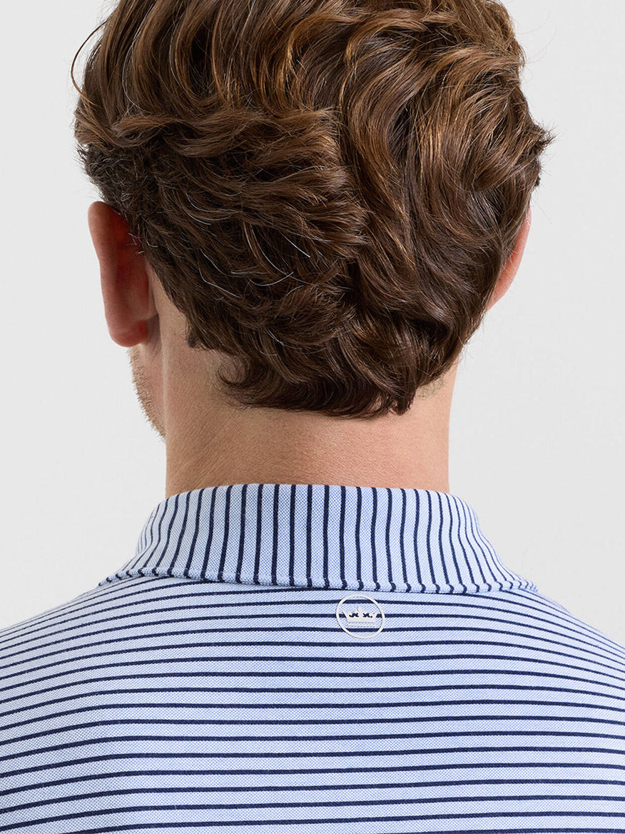 A person with brown hair is seen from behind wearing the Peter Millar Albatross Stripe Cotton-Blend Piqué Polo in Dusk Blue, which features blue and white stripes and a small round logo at the back of the neck.