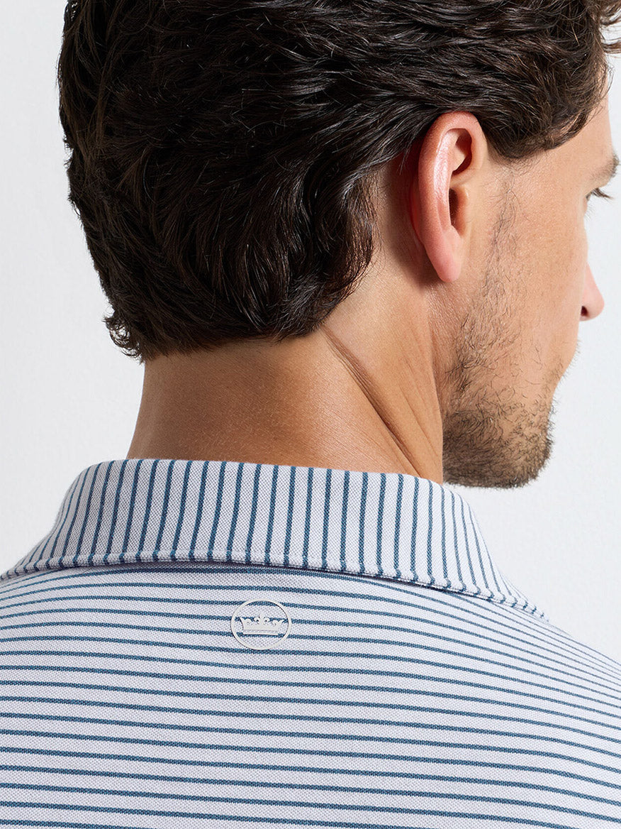 A man with dark hair is seen from behind wearing the Peter Millar Albatross Stripe Cotton-Blend Piqué Polo in Gale Grey, which features white and blue stripes, soft pima cotton-blend fabric, and a small circular logo on the collar's back.