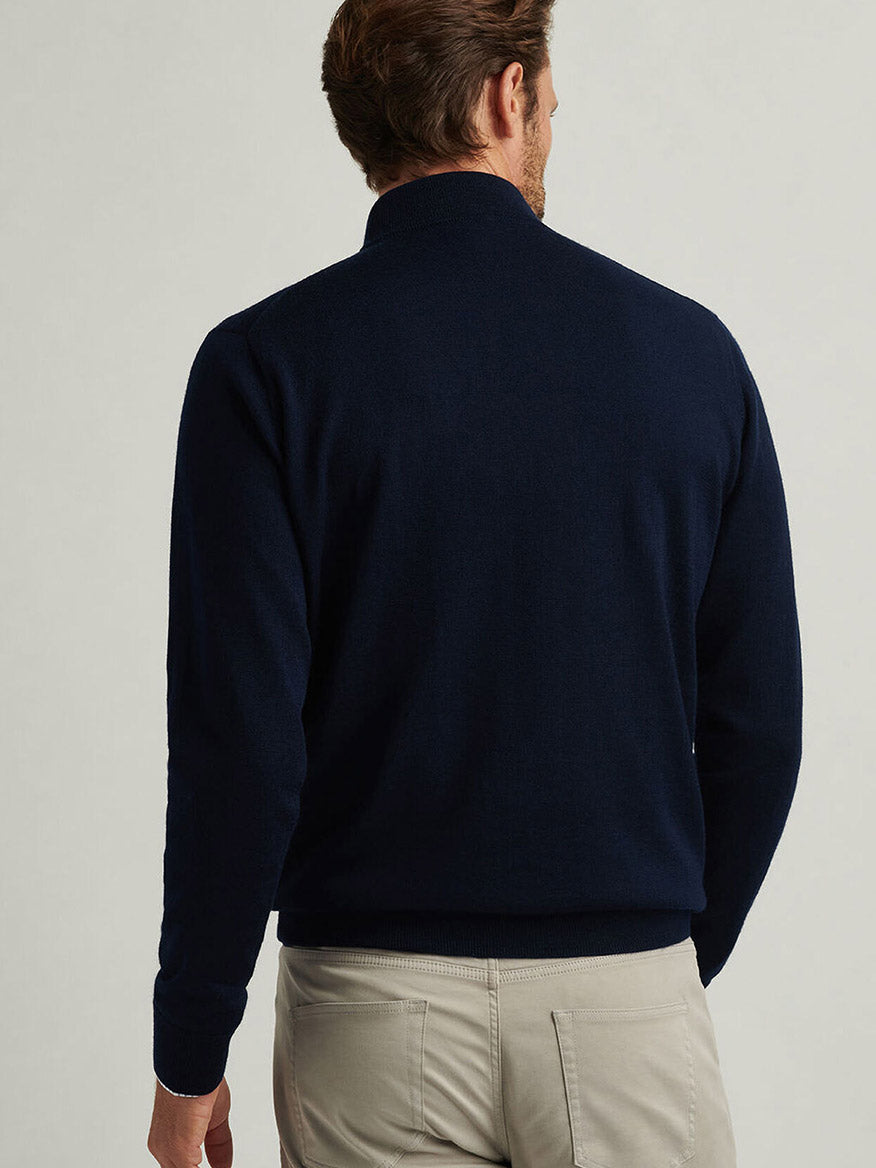 A man faces away from the camera, wearing the Peter Millar Autumn Crest Quarter-Zip in Navy and light beige pants against a plain background.