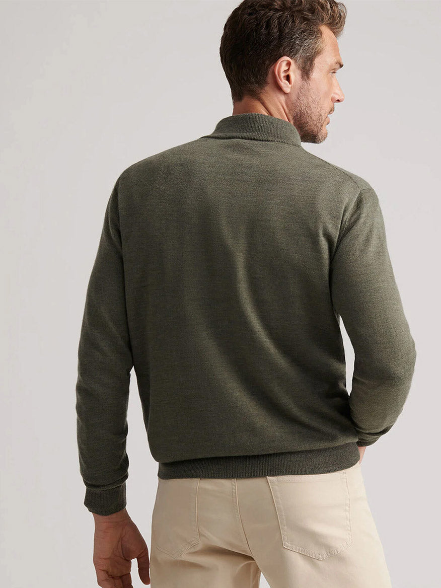 A man faces away from the camera, wearing the Peter Millar Autumn Crest Suede Trim Quarter-Zip in Basil and light beige pants against a plain background.