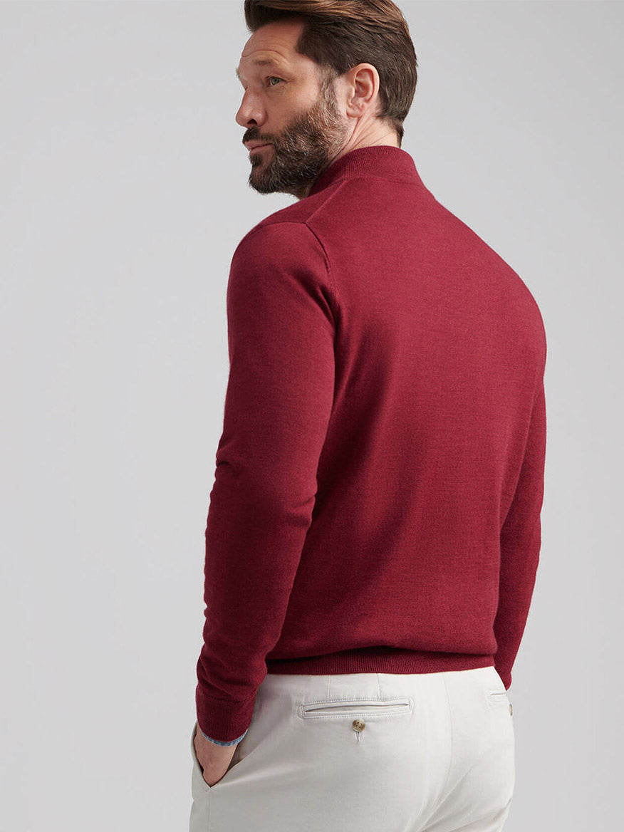 Man seen from behind wearing a Peter Millar Autumn Crest Suede Trim Quarter-Zip in Brick Red and light-colored pants, standing against a plain light background.