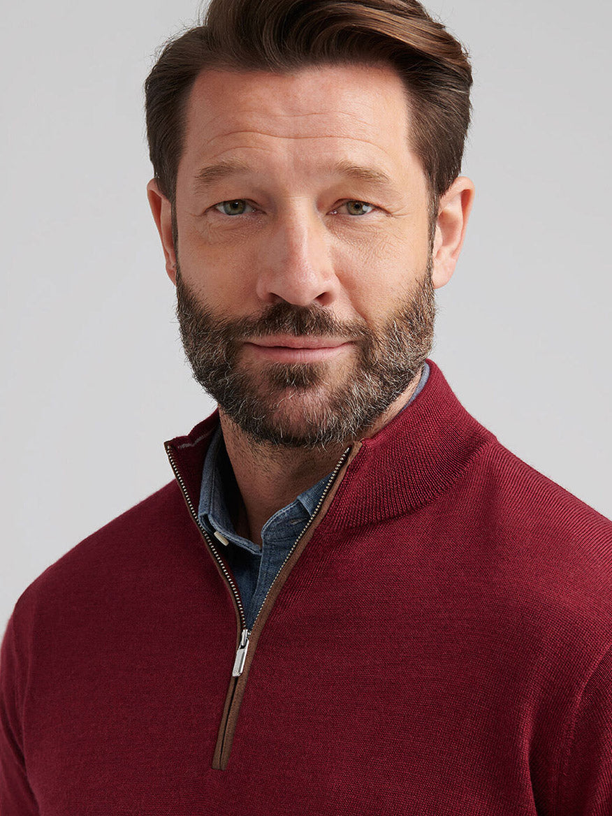 A man with short brown hair and a beard wears the Peter Millar Autumn Crest Suede Trim Quarter-Zip in Brick Red over a blue collared shirt, looking at the camera against a plain background.