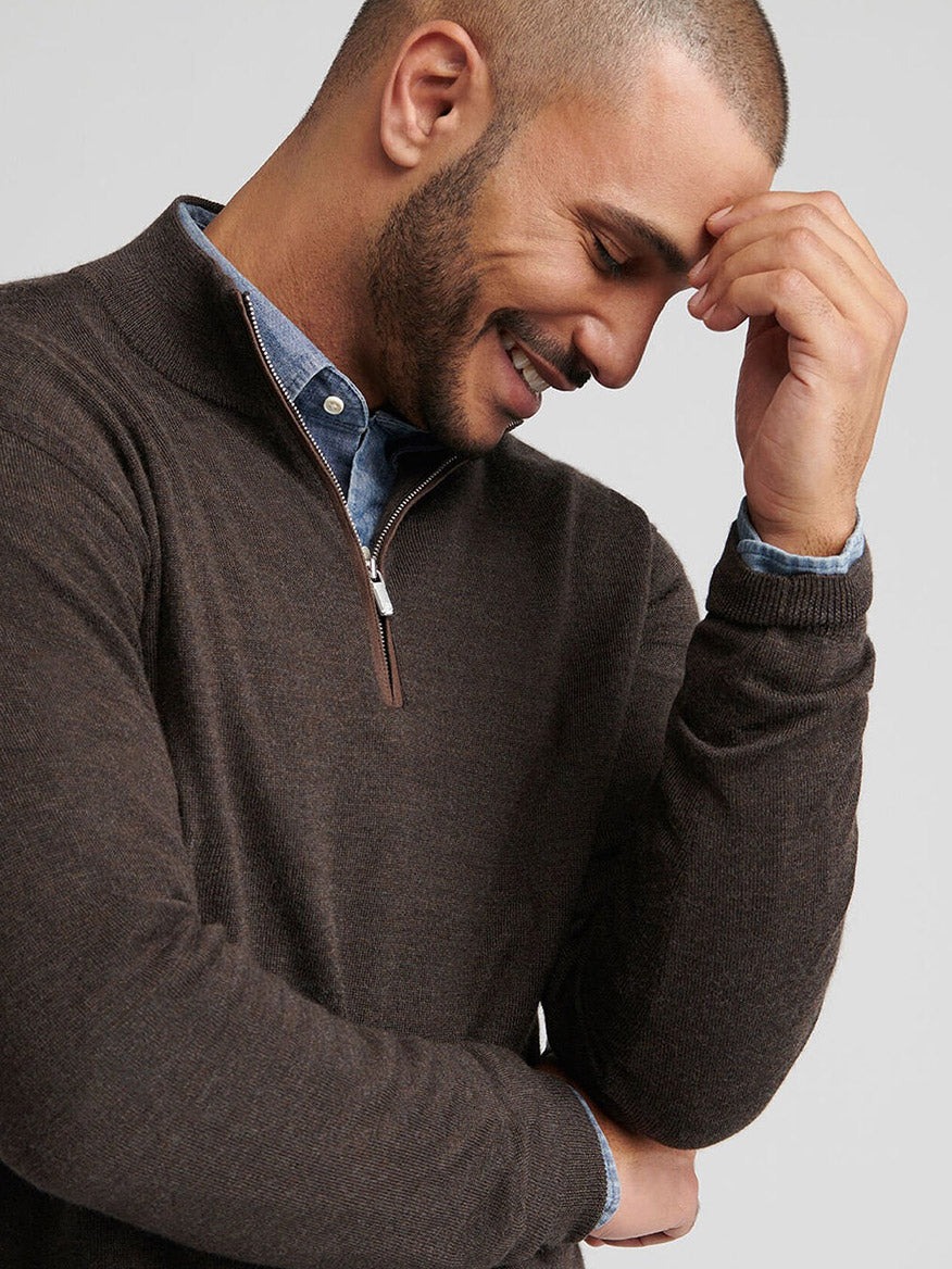 Man wearing the Peter Millar Autumn Crest Suede Trim Quarter-Zip in French Press over a blue collared shirt, smiling and touching his forehead with his right hand.