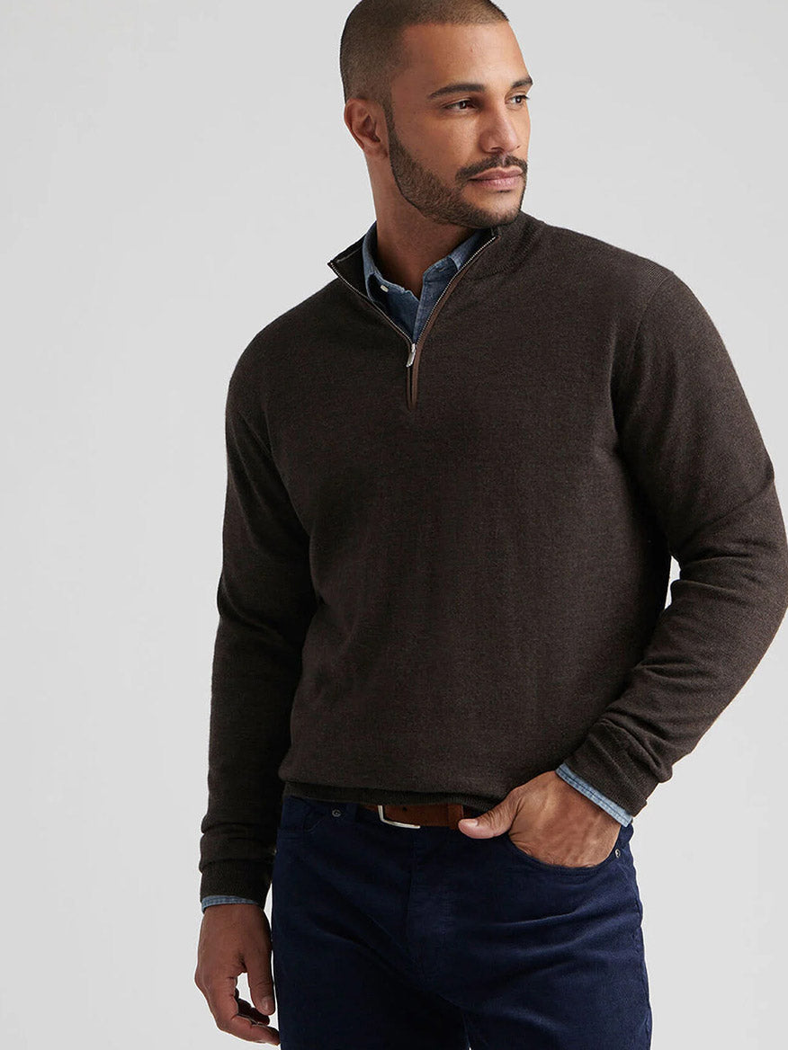 A man wearing the Peter Millar Autumn Crest Suede Trim Quarter-Zip in French Press over a blue collared shirt and navy pants stands with one hand in his pocket, looking to the side.