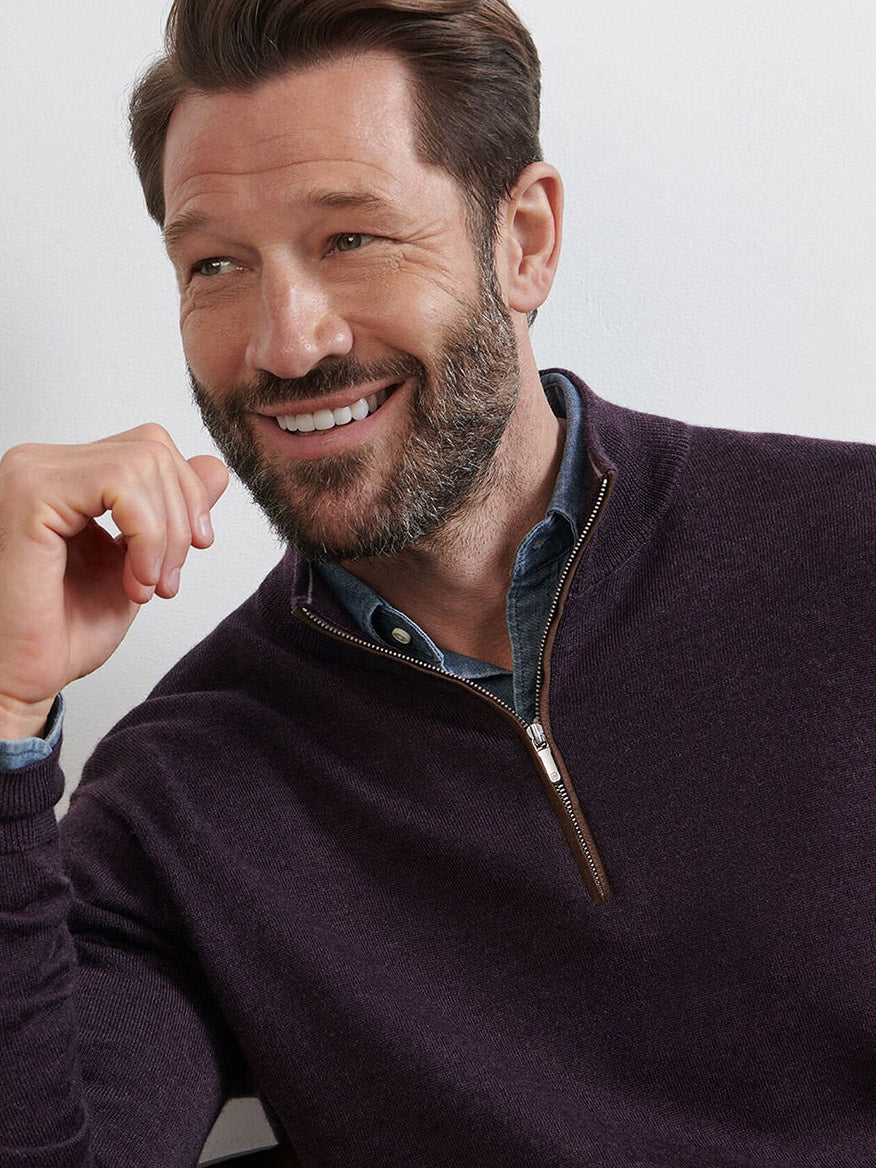 A bearded man smiles while seated, wearing the Peter Millar Autumn Crest Suede Trim Quarter-Zip in Midnight Grape, styled over a collared shirt.
