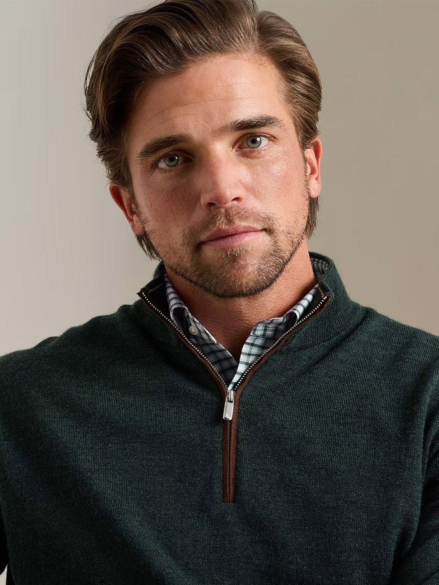 A man with light brown hair and a beard, wearing the Peter Millar Autumn Crest Suede Trim Quarter-Zip in Pine Brook over a checked shirt, is posed against a neutral background.